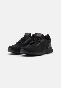 Black athletic shoes made of mesh material, featuring a textured surface, flexible sole, and front lace closure with a pull tab at the heel.