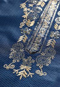 Blåt stof med indviklet gyldent blomsterbroderi og palietdetaljer langs et centralt lodret panel.