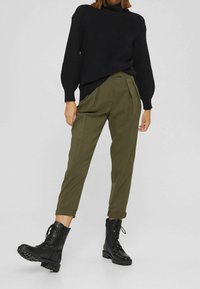 Czarny dziergany sweter z długimi rękawami, oliwkowe plisowane spodnie i czarne sznurowane botki na masywnych podeszwach.