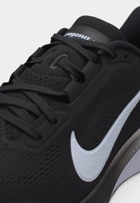 Μαύρο παπούτσι για τρέξιμο Nike με λευκό λογότυπο Swoosh, λεπτομερείς κορδόνια και επάνω μέρος από αεριζόμενο δίχτυ σε κοντινή λήψη.