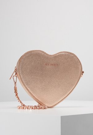 Sac bandoulière en forme de cœur en or rose texturé avec bandoulière chaîne, posé sur une surface blanche sur fond gris clair.