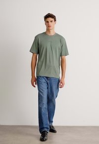 Oliven grøn bomulds T-shirt med afslappet pasform og korte ærmer, parret med lige ben jeans i blå denim. Enkel design, ingen mønstre.