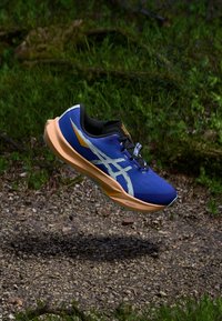Sport Schuh mit einem blauen Mesh-Obermaterial, orangefarbener Sohle und weißen Logoakzenten. Leichtes Design mit runder Form und strukturiertem Oberflächendesign.