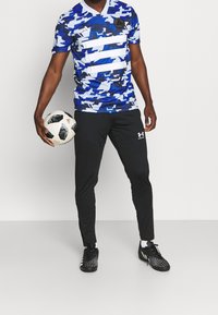 Blauw en wit camouflage patroon sportshirt, met korte mouwen en een V-hals. Gecombineerd met zwarte rekbare sportbroeken en gespotte zwarte schoenen.