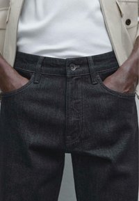Black denim jeans with contrast stitching, front pockets, and a single button closure. Fabric texture appears sturdy and smooth.
