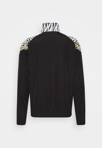 Chaqueta negra con mangas largas, cuello alto y acentos de estampado animal en blanco y marrón claro en los hombros. Tela suave con puños elásticos.