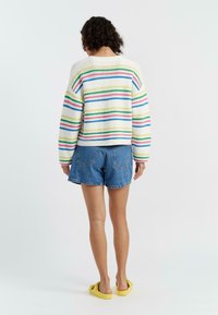 Pull en maille rayé crème, avec des rayures horizontales colorées. Associé à un short en jean. Les chaussures sont des sabots jaunes.