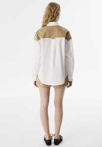 Hemd in Weiß und Beige mit Color-Blocking, langen Ärmeln, glatter Textur, abgerundetem Saum und einem dezenten Branding-Detail auf der Rückseite.