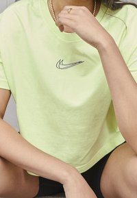 Ljusgrön, kortärmad t-shirt i mjuk bomull, med en svart Nike-logga. Modellen sitter med en hand vilande på sin hakan.