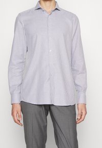 Chemise à manches longues à carreaux blancs et bleu marine avec un col boutonné, présentant une coupe droite et une texture lisse. Boutons argentés visibles.