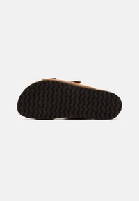 Zapato de ante marrón con suela de goma que presenta un patrón de banda de rodadura en zigzag. El diseño incluye dos correas ajustables.