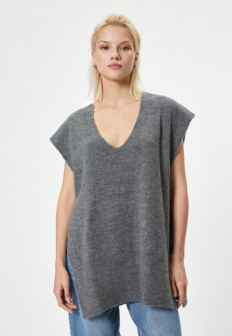 Maglione grigio lavorato a maglia con maniche corte, scollo a V profondo, vestibilità rilassata e texture morbida; l'orlo presenta un leggero design a scendere.