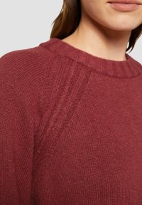 Pull en maille bordeaux avec un col côtelé et des détails texturés subtils sur les épaules. Tissu doux de poids moyen.