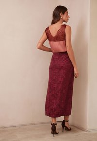 Bordó színű, virágmintás maxi ruha csipkés felsőrésszel, V-alakú hátkivágással, szatén derékrésszel és testhez simuló szabással. Barna, magas sarkú cipővel párosítva.