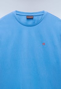 Hellblaues T-Shirt mit Rundhalsausschnitt und kleinem Logo der norwegischen Flagge in Rot, Weiß und Blau auf der linken Brust.