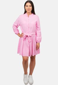 Abito rosa a camicia con cintura in vita, maniche lunghe, tessuto strutturato e gonna svasata. Abbinato a sneakers bianche.