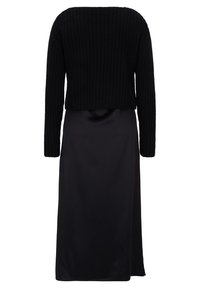 Schwarzer, kurzer, gestrickter Pullover mit langen Ärmeln, kombiniert mit einem eleganten, schwarzen Satin-Maxikleid. Glatte Textur mit einer taillierten Silhouette.