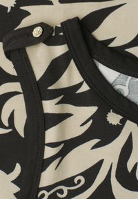 Tissu à motif floral noir et beige avec bordure noire et petit bouton-pression métallique sur la couture de l'épaule.