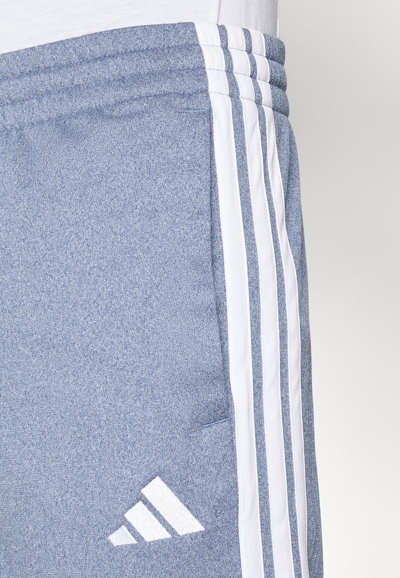 Jogging léger bleu fabriqué en tissu doux. Présente des rayures verticales blanches et un logo Adidas en blanc en bas à gauche.