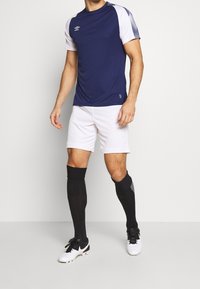 Námořnická a bílá sportovní dres s krátkými rukávy, spárovaný s bílými šortkami a černými punčochami k kolenům. Obsahuje logo na hrudi.