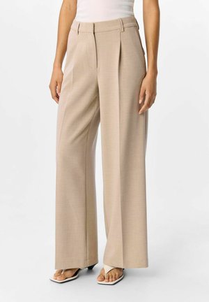 Pantalones de pierna ancha beige con pliegues, hechos de una tela texturizada. Presentan una cintura alta y sutiles bolsillos laterales, combinados con sandalias blancas.