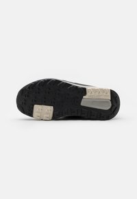 Suela de zapatilla de trail en negro y gris claro con goma texturizada para mayor agarre, que presenta una punta ancha y un área del talón reforzada. Destacada con el logo 'TRAXION'.