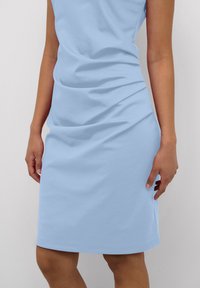 Blaues baumwollenes ärmelloses Kleid mit einer figurbetonten Form und weicher Textur; weist dezente Drapierungen an der Taille und einen geraden Saum auf.