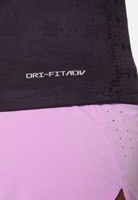 Gros plan sur le détail du tissu noir Dri-FIT ADV au-dessus d’un short de sport violet clair avec de petits trous de ventilation et une fente latérale.