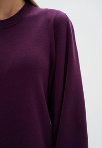 Lila tröja med ribbat halsband, gjord av strukturerat stickat tyg, med långa ärmar och avslappnad passform.