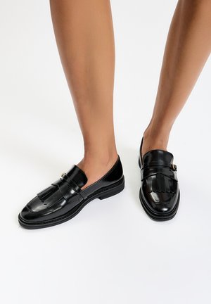 Black leather loafers with a fringed design and a decorative buckle. Features a rounded toe and flat rubber sole for stability.