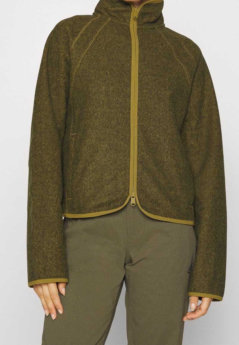 Veste polaire verte avec un col montant, une fermeture éclair à l'avant et un bord contrastant jaune. Présente un motif texturé et une silhouette courte.