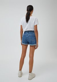 Pantalones cortos de mezclilla con un ajuste relajado, con una cintura alta y dobladillo enrollado, combinados con una camiseta blanca de manga corta y lisa.