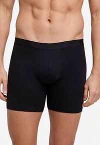 Czarne bokserki o dopasowanym kroju z elastycznym pasem, na którym znajduje się nazwa marki. Gładka tkanina, długość do połowy uda.