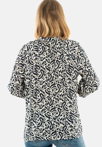 Blusa a maniche lunghe con sfondo crema e motivi astratti blu navy che si avvolgono. Tessuto morbido con taglio rilassato e scollo arricciato.