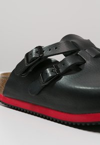 Schwarze Ledersandale mit zwei verstellbaren Riemen, schwarzen Schnallen und einer roten Gummisohle. Verfügt über ein Korkfußbett für zusätzlichen Komfort.
