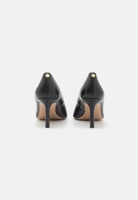 Scarpe nere in pelle con tacco alto e punta affilata, caratterizzate da un piccolo accento dorato sul retro, una superficie liscia e un tacco a stiletto sottile.