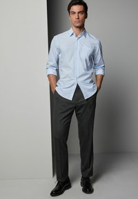 Chemise boutonnée à rayures bleu clair avec manches longues, associée à un pantalon noir taillé et des chaussures de ville noires. Apparence propre et formelle.