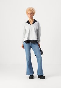 Grå V-hals sweatshirt lagd over en svart skjorte med hvite prikker, paret med lyseblå buede jeans og svarte plattform sko.