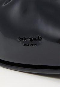 Must must sukileva käekott mustast patendinahast, millel on sile tekstuur ja pressitud "kate spade NEW YORK" logo. Omab puhtaid jooni ja struktureeritud kuju.