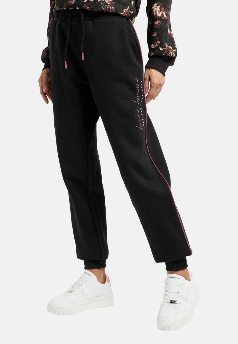 Zwarte joggers met roze zijkanten, voorzien van een elastische tailleband en opgerolde enkels. Gecombineerd met witte sneakers met roze details.