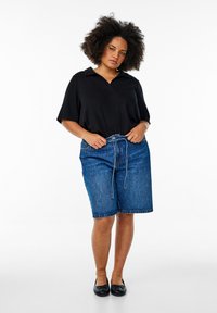 Svart kortärmad topp med krage, i kombination med blå denimshorts med knytning i midjan. Outfiten kompletteras med svarta platta skor.