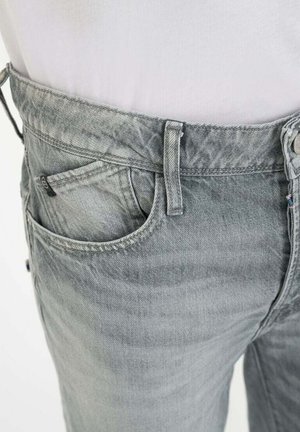 Vaqueros de mezclilla grises, con un corte regular, diseño de cinco bolsillos, trabillas para cinturón y una sutil textura de desgaste en la tela.