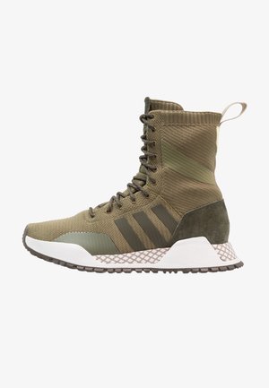 Wysokie buty sportowe w kolorze oliwkowej zieleni wykonane z dzianiny, z przodu sznurowane, z trzema ciemnymi paskami, teksturowaną podeszwą i pętelką na pięcie.