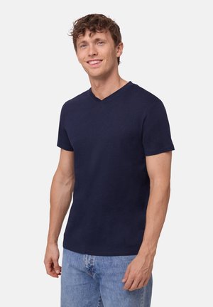 Marinblå V-hals t-shirt med kort ärm, gjord av mjukt tyg. Bärs med ljusblå jeans, som visar upp en figurnära silhuett.