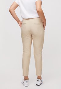 Světle béžové kalhoty s hladkým povrchem, dvěma zadními kapsami a ke snížené nohavici, doplněné bílými teniskami.