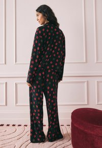 Must musta komplekt, mis sisaldab laia lõikega särki ja pükse, kaunistatud punaste ja roheliste huulemustritega. Pehme kangas ja mugav siluett.