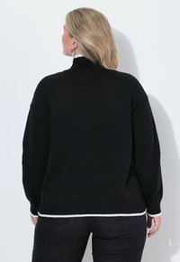 Maglione nero lavorato a maglia con collo alto e orlo a coste, caratterizzato da un accento bianco sul fondo. Vestibilità oversize con maniche lunghe.