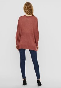 Løs, letvægts trøje i rustfarve med lange ærmer, ribbet kant og sideslidser, kombineret med mørke skinny jeans og høje hæle.