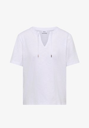 Biała koszulka z krótkim rękawem, dekoltem w serek i troczkami, z subtelną fakturą oraz małą metką marki w pobliżu brzegu.