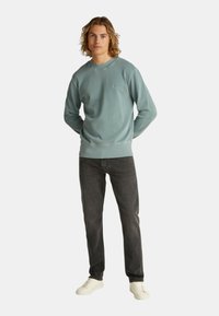 Felpa azzurra chiara con colletto e polsini a costine, abbinata a jeans scuri e sneakers bianche. Vestibilità casual, trama morbida, branding minimo.
